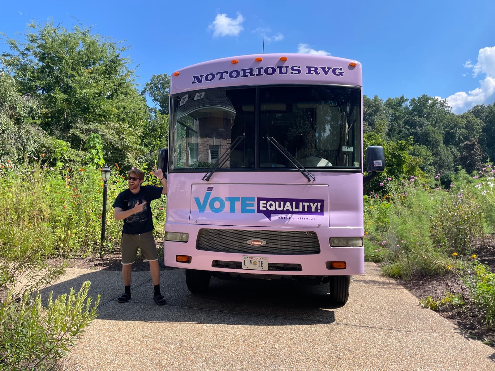 A volunteer standing beside the pink Vote Equality bus in a garden